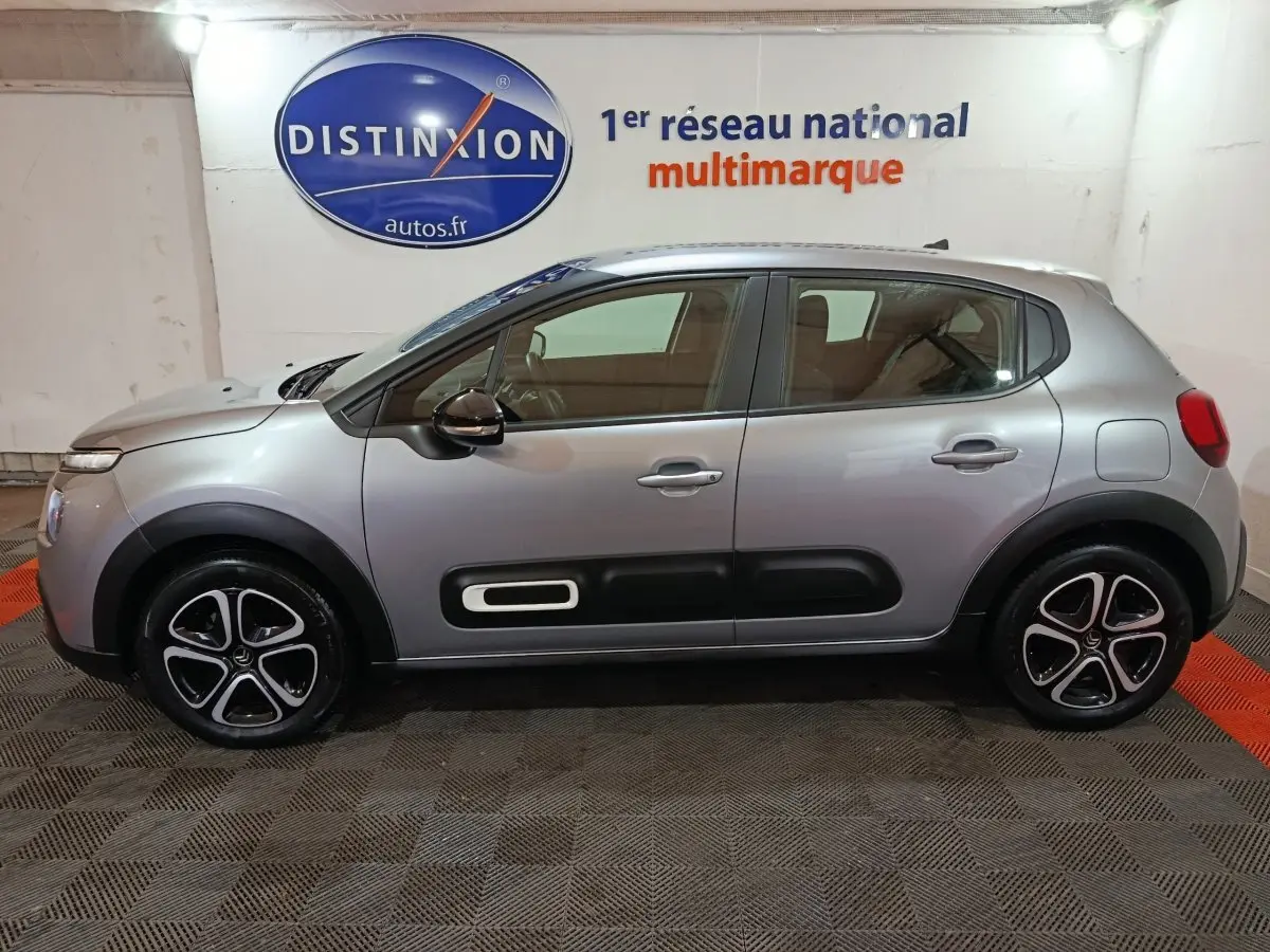Profil côté gauche d'une Citroën C3 gris clair 2024 avec protections noires et jantes distinctives en concession.