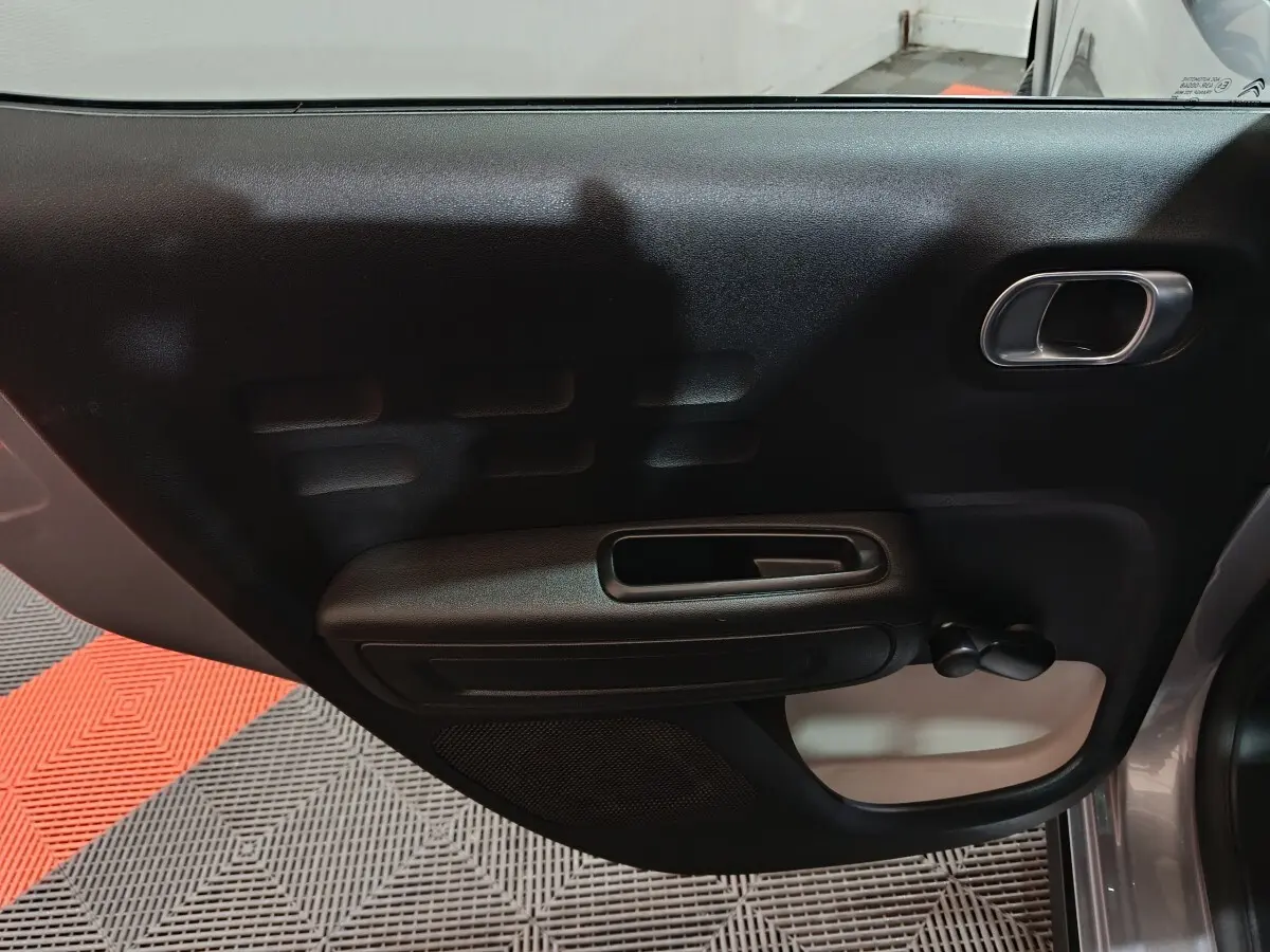 Vue rapprochée de la porte arrière droite intérieure noire d'une Citroën C3 gris clair 2024, avec poignée et manivelle de vitre.