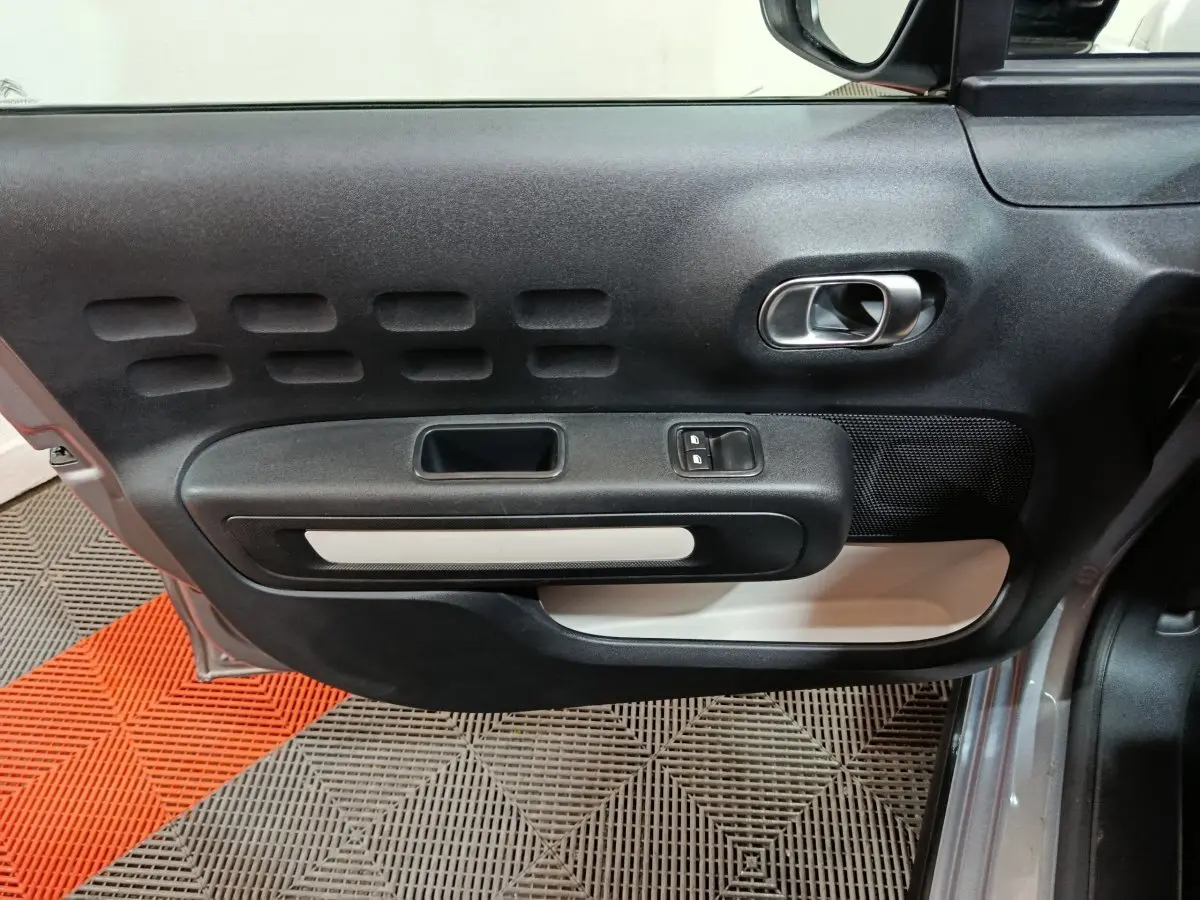 Vue latérale du panneau de porte avant gauche gris clair de la Citroën C3 2024 avec commande de vitres et poignée intégrée.