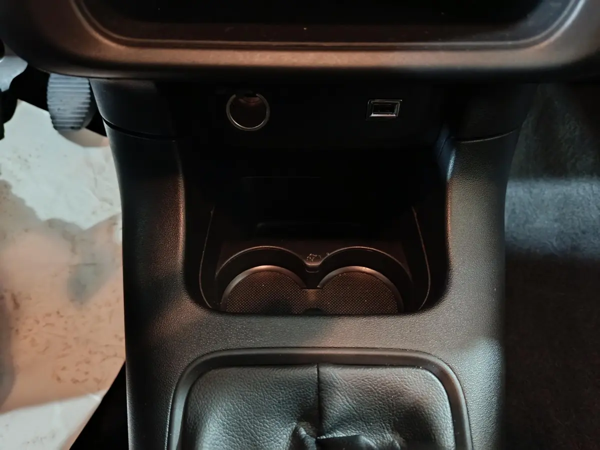 Vue rapprochée de la console centrale noire avec prise USB et porte-gobelets de la Citroën C3 BlueHDi 2024.