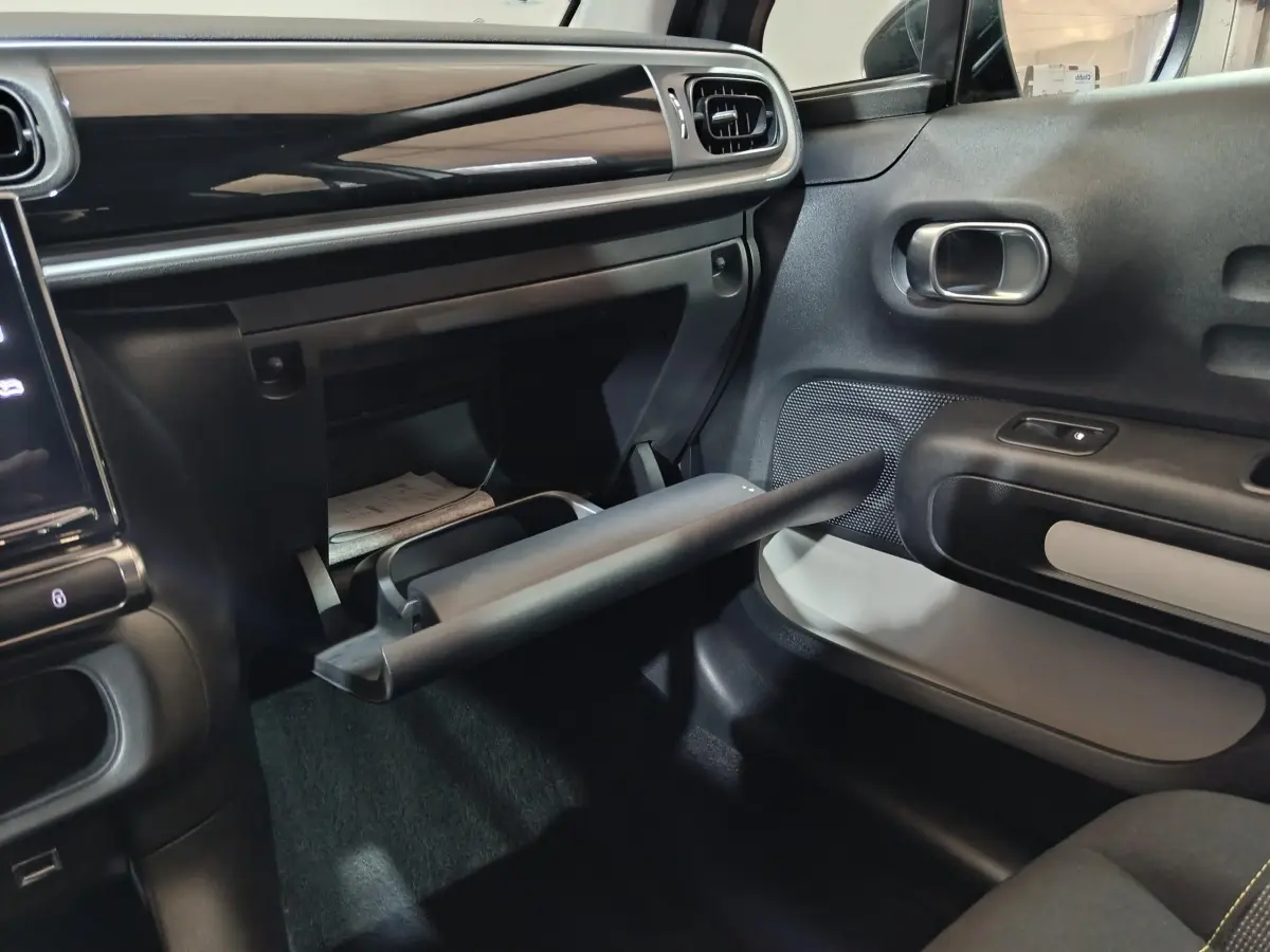 Intérieur avant droit de la Citroën C3 2024 gris clair, avec boîte à gants ouverte et tableau de bord noir brillant.