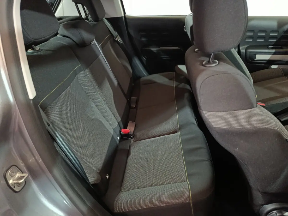 Vue intérieure côté arrière gauche de la banquette noire de la Citroën C3 2024 gris clair avec appuie-têtes et ceintures visibles.