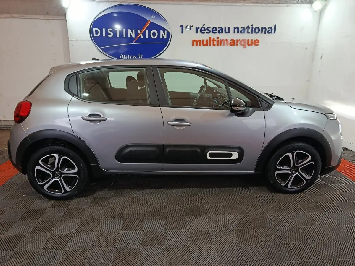 Profil côté droit d'une Citroën C3 gris clair 2024 avec protections noires sur les portières et jantes stylisées.
