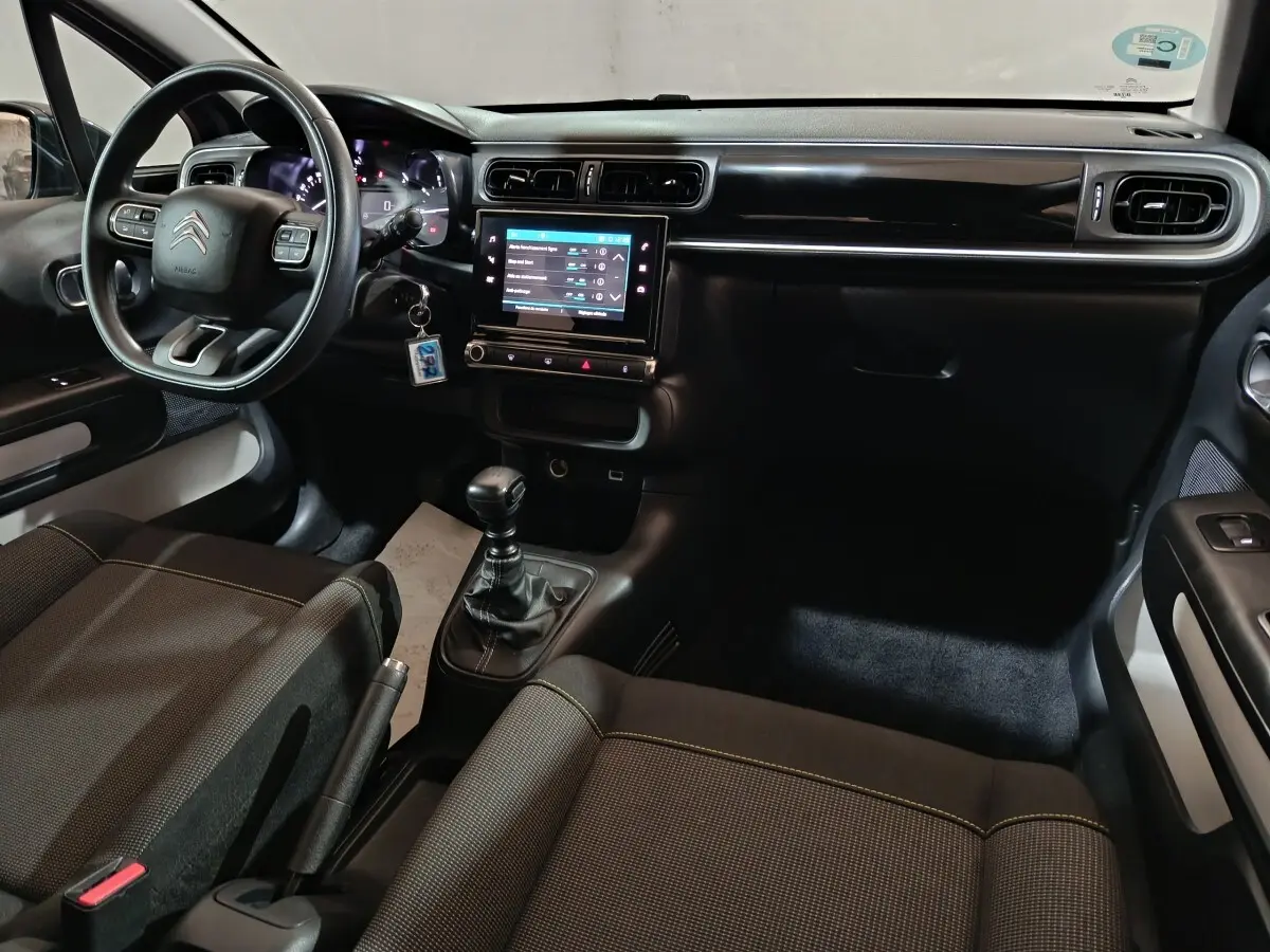 Vue intérieure avant de la Citroën C3 2024, tableau de bord noir avec écran tactile central et volant multifonctions.