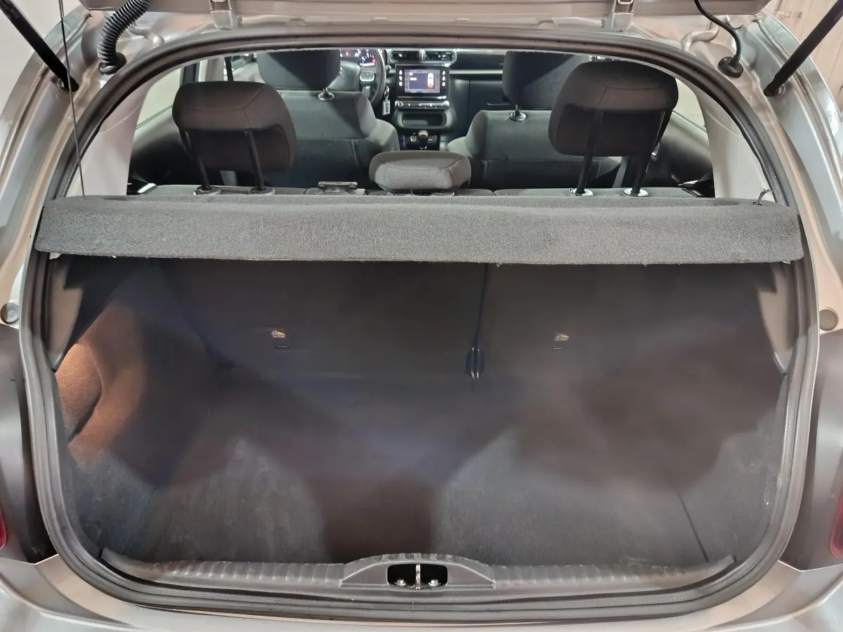 Vue arrière du coffre ouvert d'une Citroën C3 gris clair 2024, avec banquette arrière et tableau de bord visible.