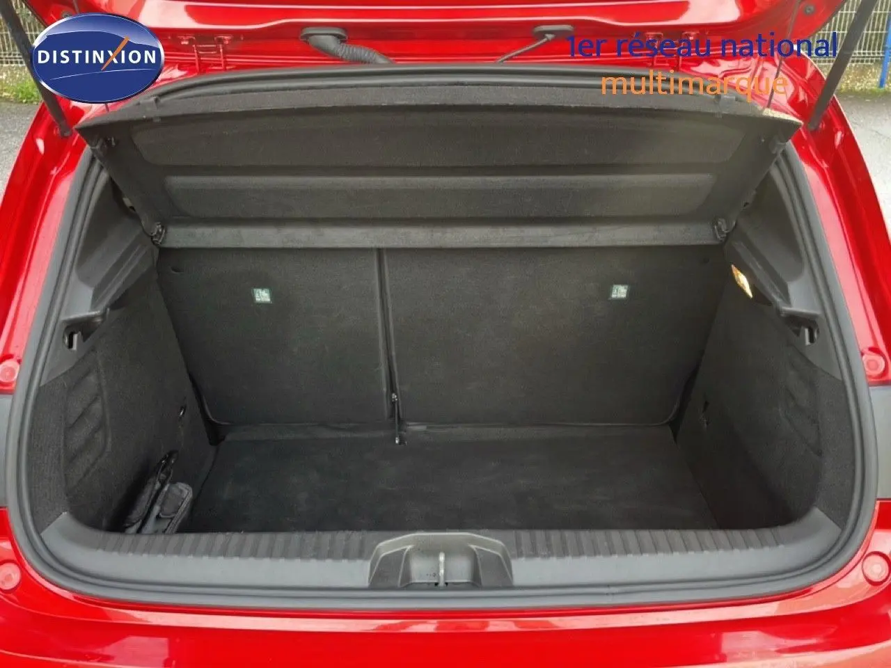 Coffre ouvert vu de l'arrière d'une Renault Clio rouge Désir Métal, montrant un espace de rangement vide et propre.