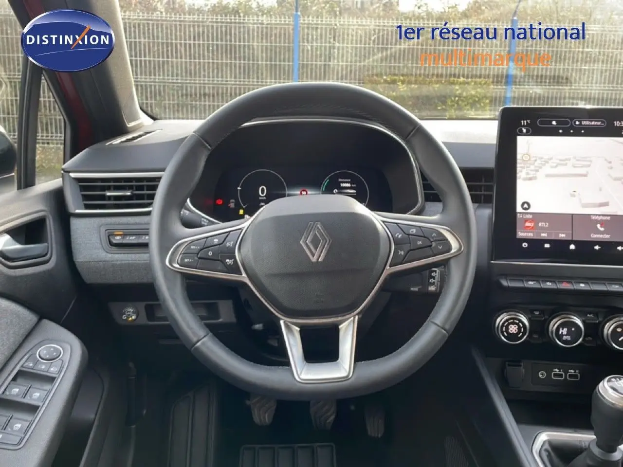 Vue intérieure centrée sur le volant de la Renault Clio rouge Désir Métal, avec tableau de bord numérique et écran tactile.
