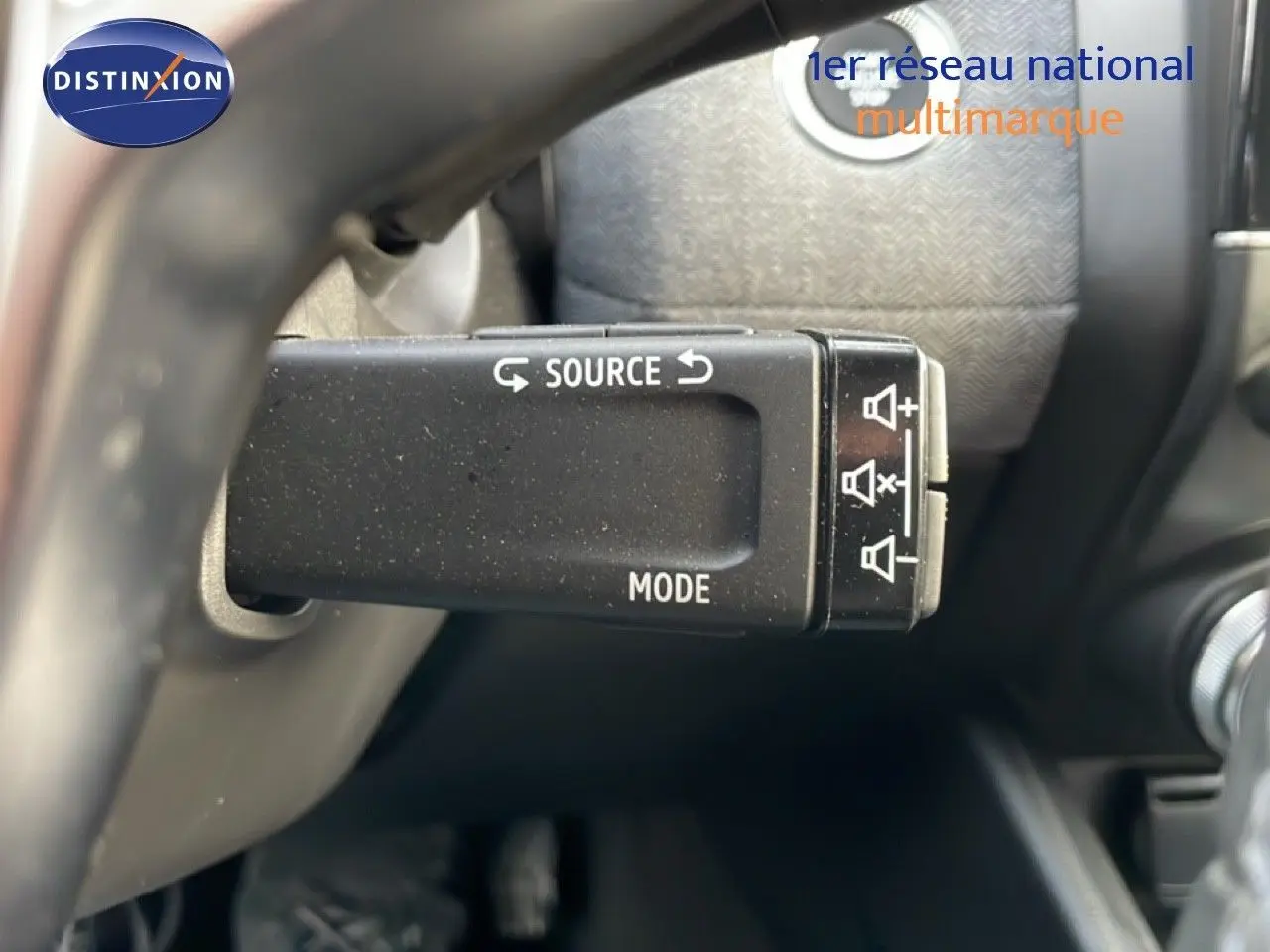 Gros plan sur la commande au volant de la Renault Clio rouge Désir Métal, mettant en valeur les boutons source et mode.