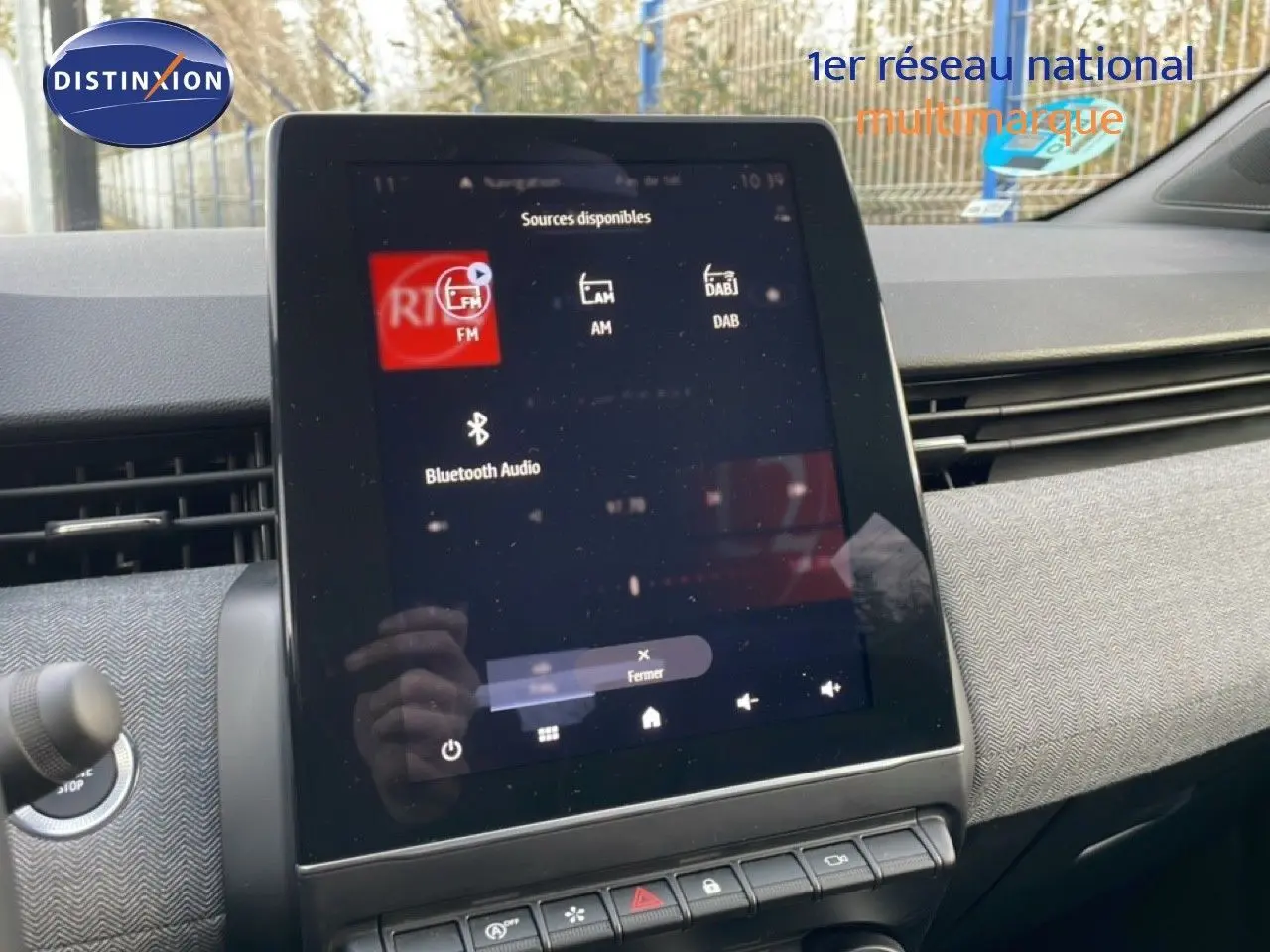 Vue intérieure centrée sur l'écran tactile multimédia de la Renault Clio 2025 avec tableau de bord gris et boutons fonctionnels.