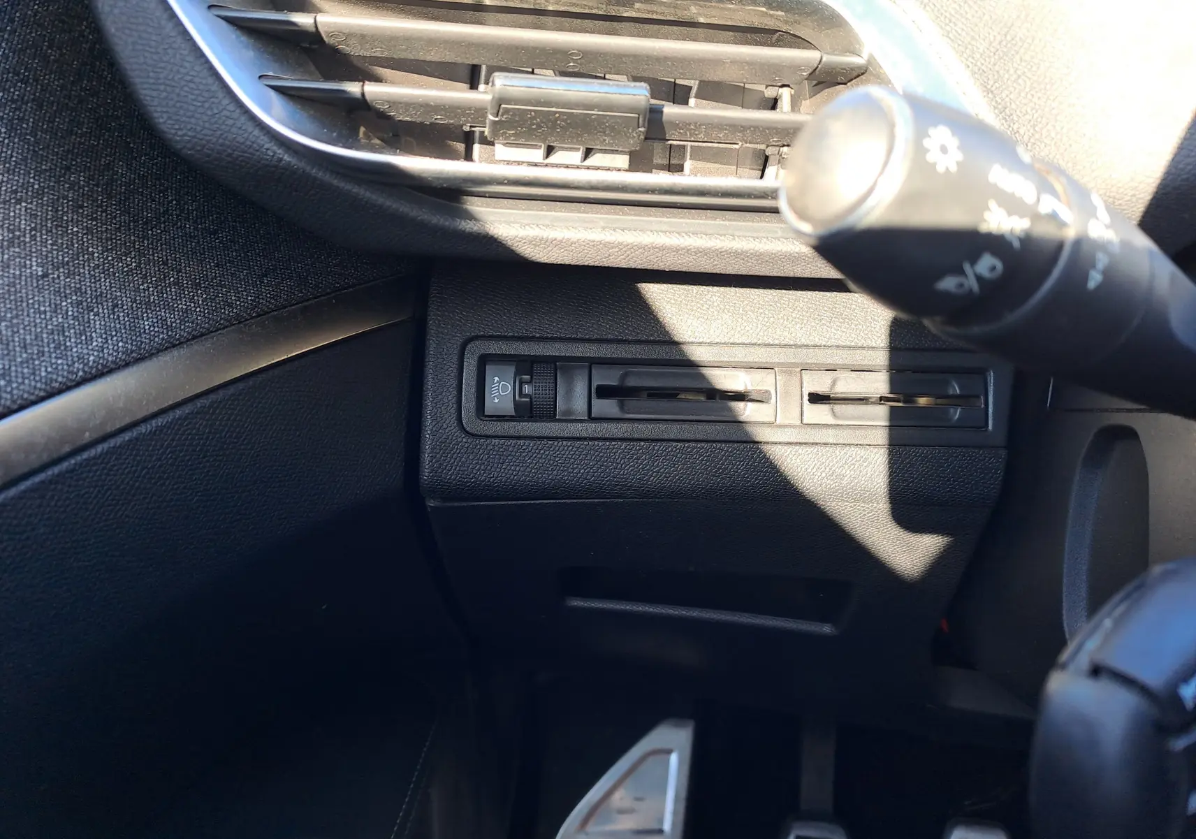 Détail du tableau de bord côté gauche avec commandes de réglage des phares et aérateurs noirs dans un Peugeot 5008 gris 2019.