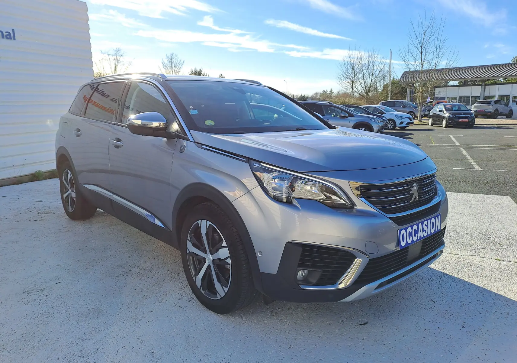 Peugeot 5008 gris vue 3/4 avant droit, SUV 7 places avec jantes alliage et calandre chromée, stationné en extérieur.