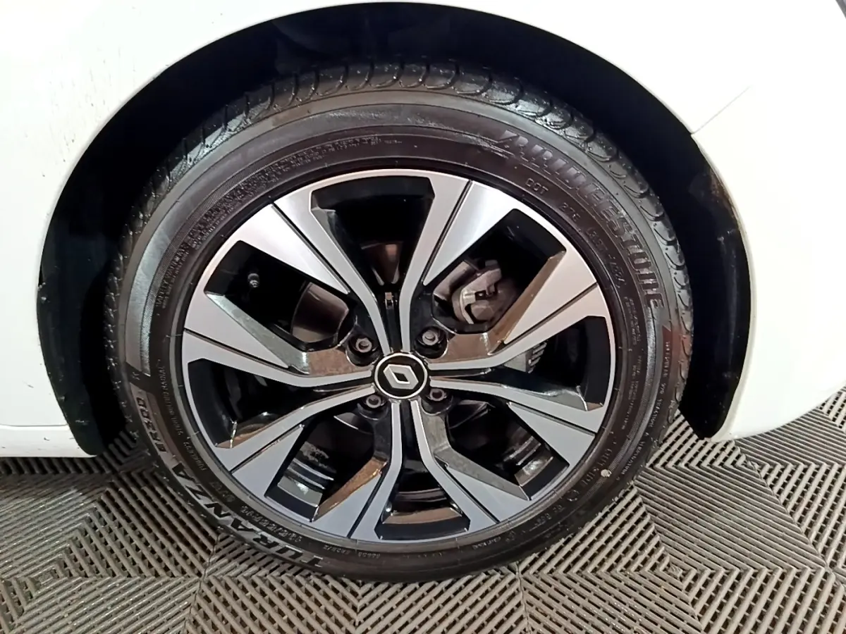 Gros plan sur la roue avant gauche d'une Renault Clio blanche avec jante alliage bicolore au design moderne.