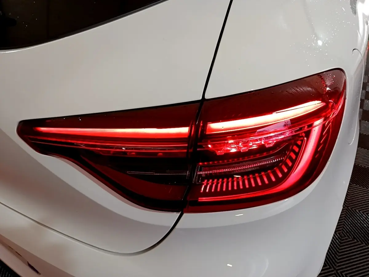 Feu arrière droit allumé sur Renault Clio Business blanc, vue rapprochée du coffre et de la carrosserie.