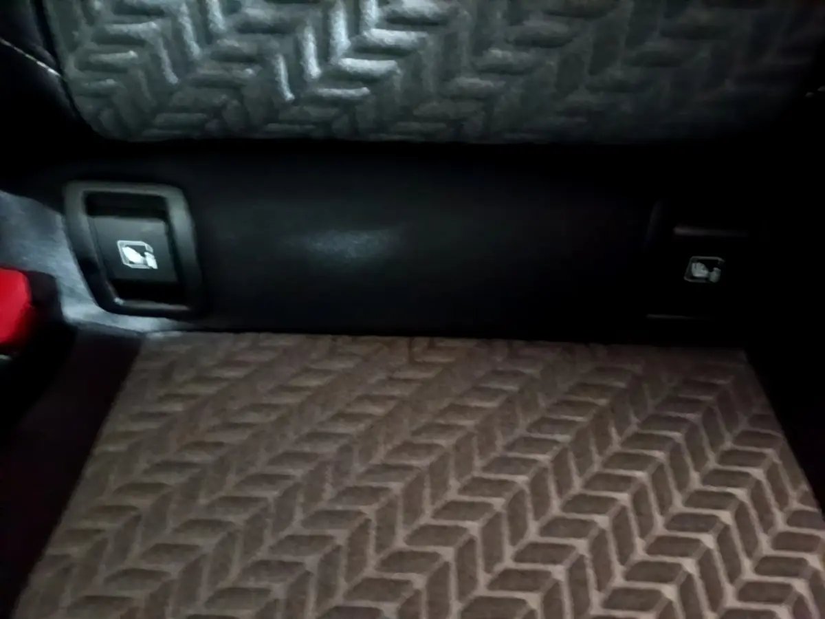 Détail du coffre de la Renault Clio Business blanc, montrant les commandes d'ouverture des sièges arrière et le tapis à motif chevrons.