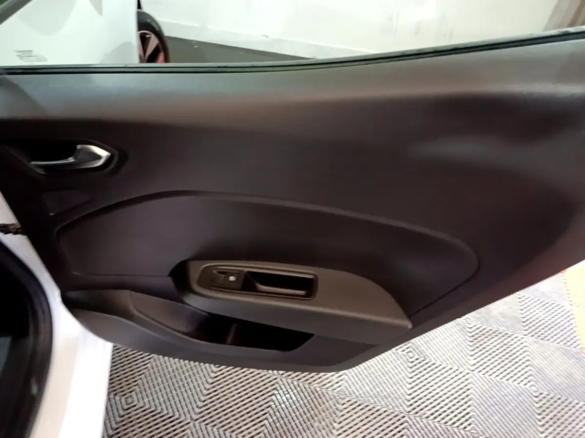 Vue rapprochée de la porte intérieure côté gauche d’une Renault Clio blanche, avec poignée et commande de fenêtre noire.