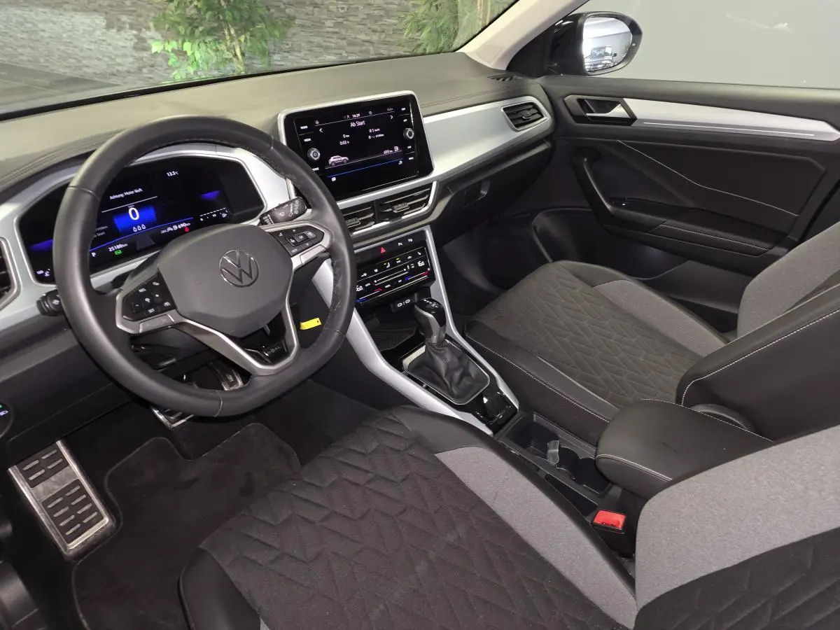 Vue intérieure côté conducteur du Volkswagen T-Roc gris 2025, avec tableau de bord digital et volant multifonction cuir.
