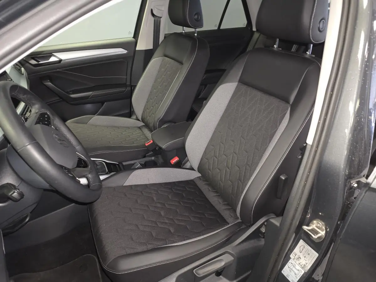 Vue intérieure côté conducteur du Volkswagen T-Roc 2025 avec sièges tissu noir et gris et accoudoir central.