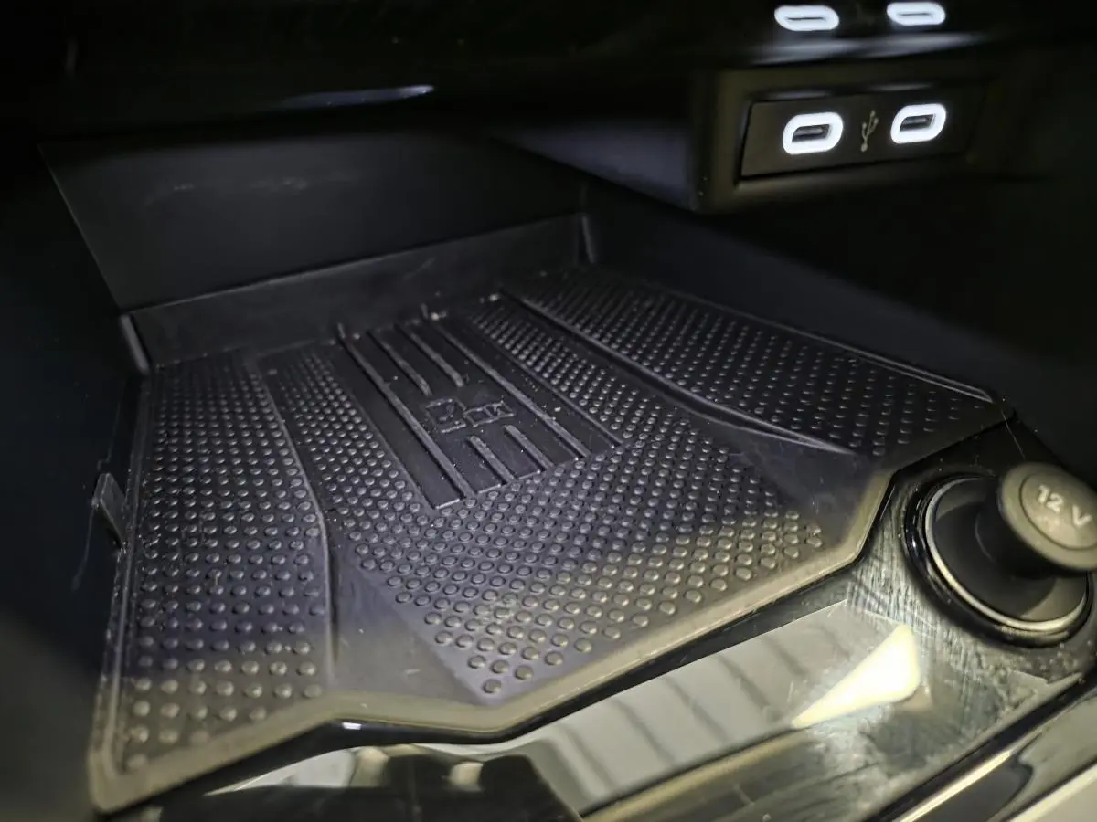 Gros plan sur le compartiment de rangement avant du Volkswagen T-Roc gris, avec ports USB-C et prise 12V visibles.