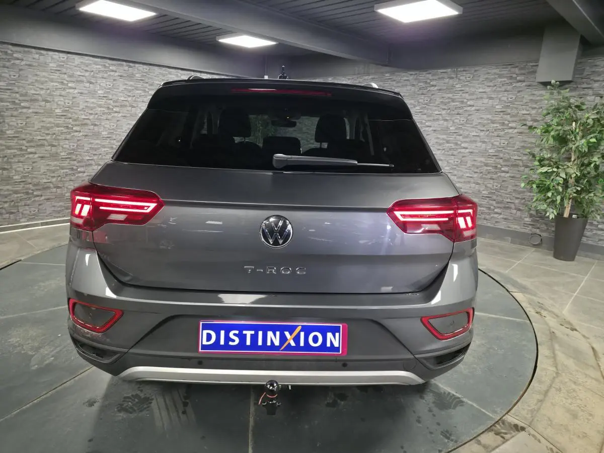 Vue arrière d'un Volkswagen T-Roc gris métallisé 2025 avec feux LED allumés et attelage démontable.