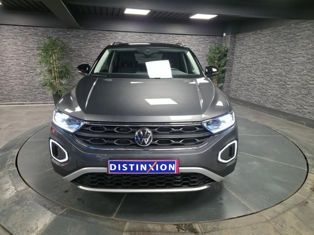 Vue de face d'un Volkswagen T-Roc gris métallisé avec feux LED allumés et calandre noire en showroom.