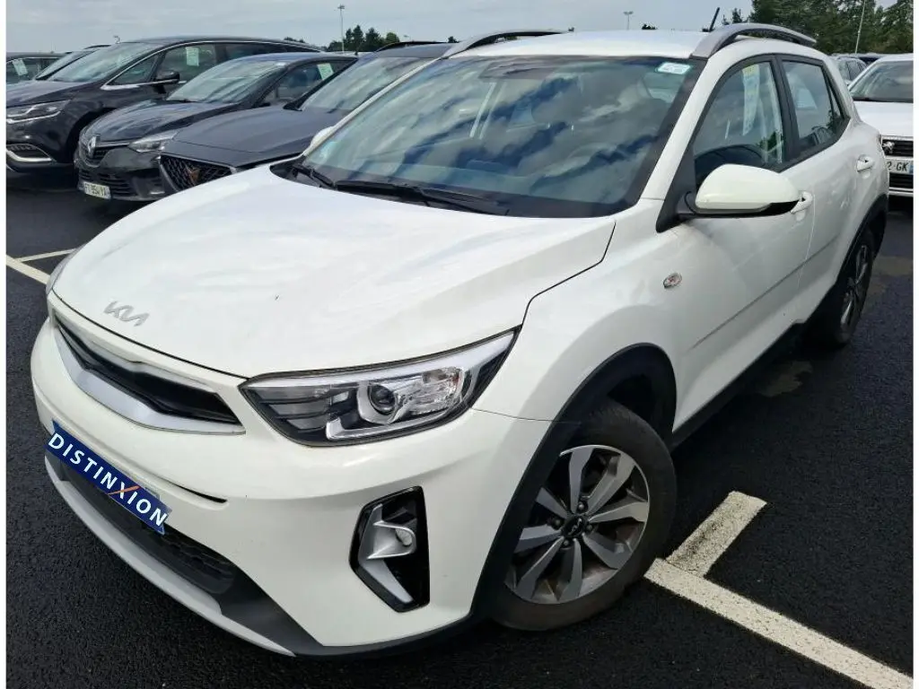 KIA Stonic blanc vue 3/4 avant droit, SUV compact avec toit noir et jantes alliage, stationné sur parking.