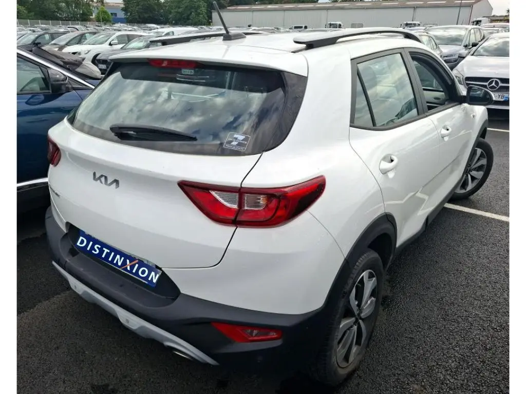 Vue 3/4 arrière droite d'un Kia Stonic blanc 2022 avec feux arrière rouges et toit avec barres de toit noires.