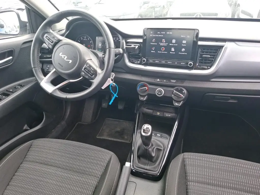 Vue intérieure avant du Kia Stonic blanc 2022, avec volant multifonction, écran tactile et levier de vitesses manuel.