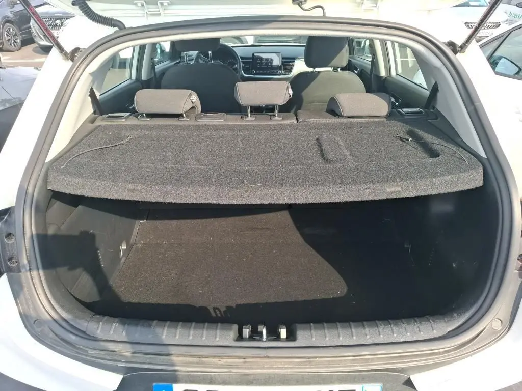 Coffre ouvert vu de l'arrière d'un KIA Stonic blanc 2022, avec cache-bagages en place et sièges arrière visibles.