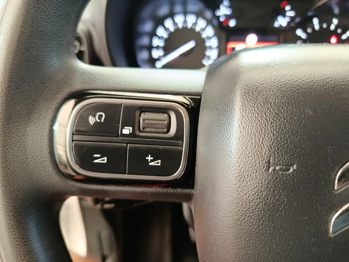 Gros plan sur les commandes gauche du volant noir du Citroën Berlingo 2020, avec tableau de bord flou en arrière-plan.