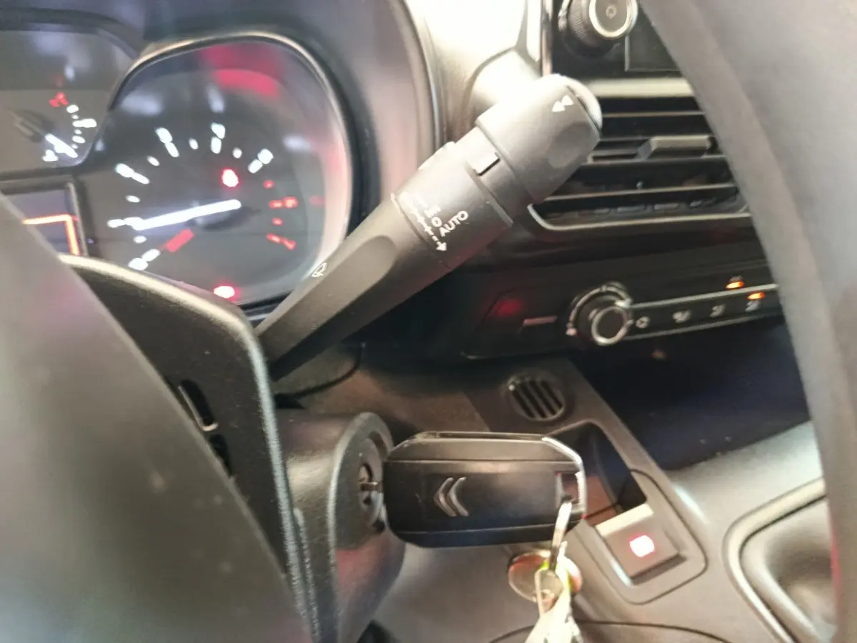Gros plan intérieur sur le volant et le tableau de bord noir du Citroën Berlingo blanc, clé insérée dans le contact.