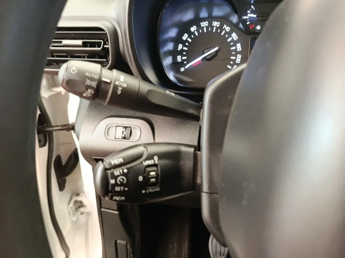 Gros plan sur le volant multifonctions et les commandes de régulateur de vitesse du Citroën Berlingo blanc, tableau de bord visible.
