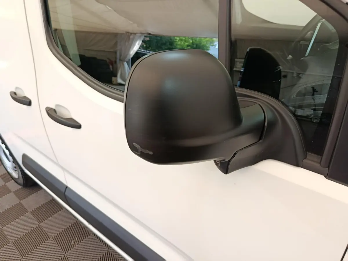 Rétroviseur noir en gros plan côté gauche d’un Citroën Berlingo blanc, vue partielle sur la porte avant.