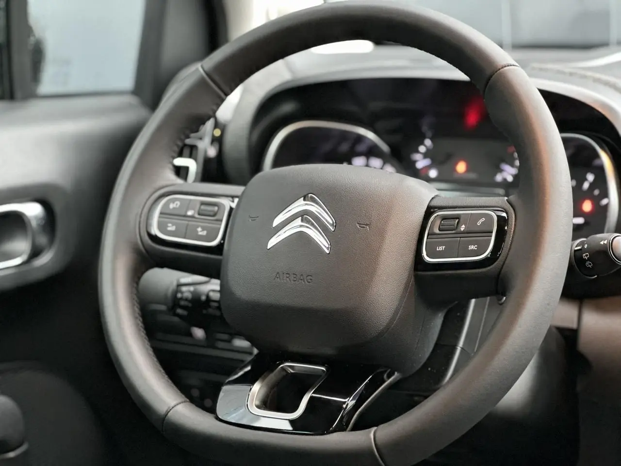 Volant en croûte de cuir noir avec commandes intégrées, tableau de bord flou en arrière-plan d'une Citroën C3 Aircross 2024.