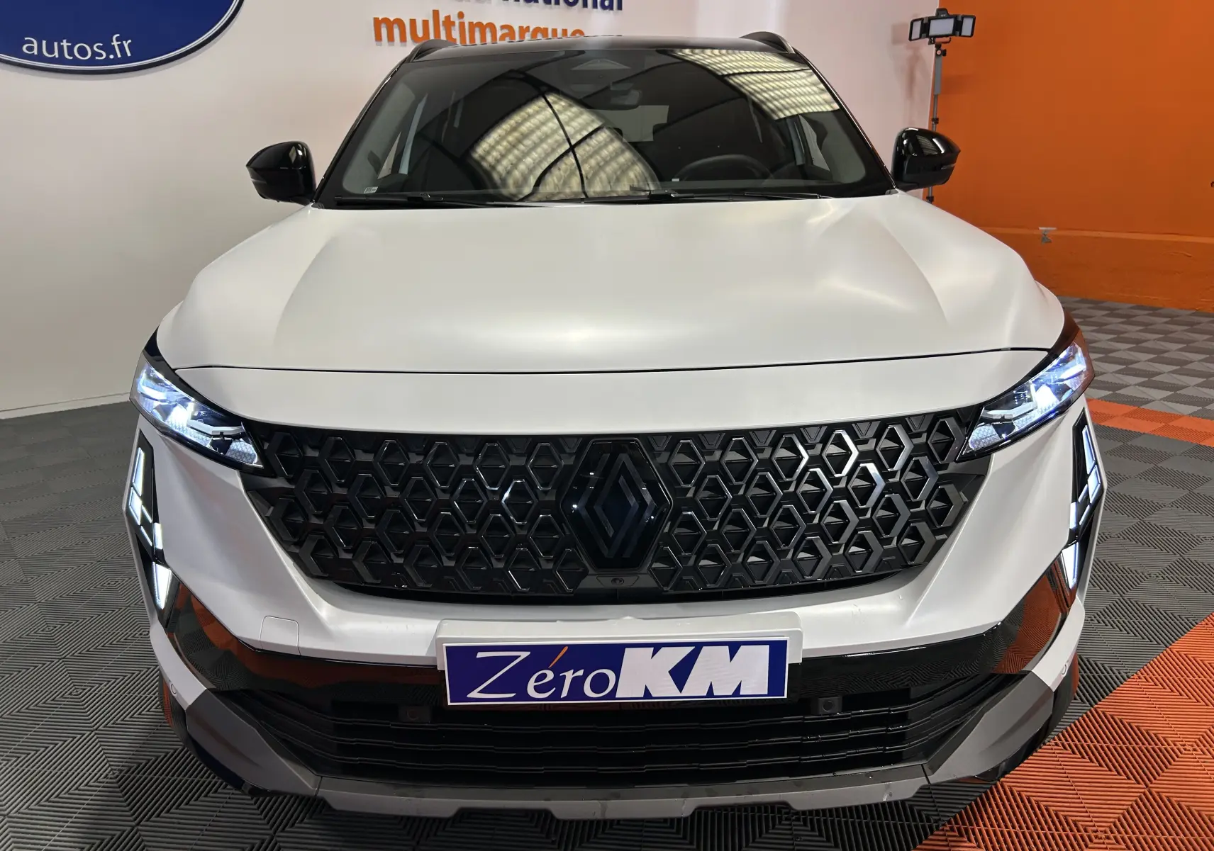 Vue frontale d'un Renault Austral blanc nacré satin avec calandre noire à motif hexagonal et phares LED allumés.