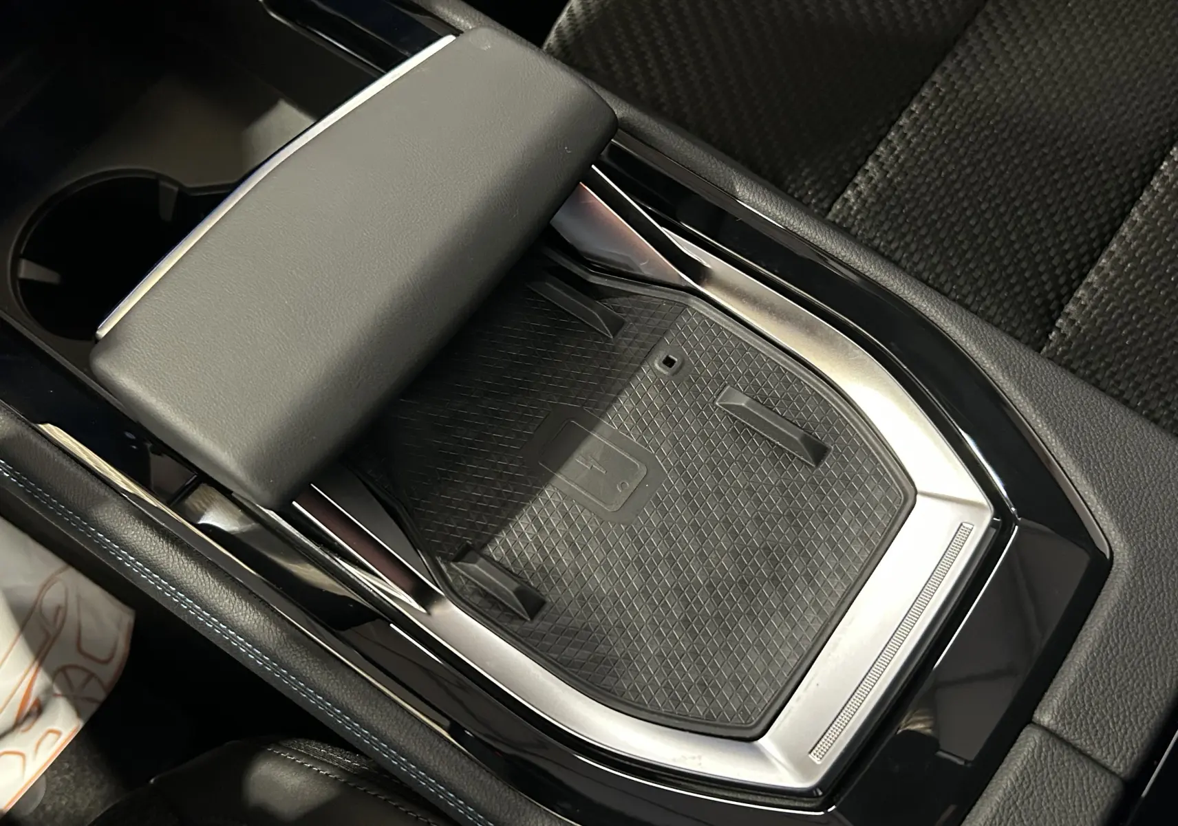 Gros plan sur la console centrale noire du Renault Austral Ph.2 avec surface de charge sans fil et accoudoir cuir.