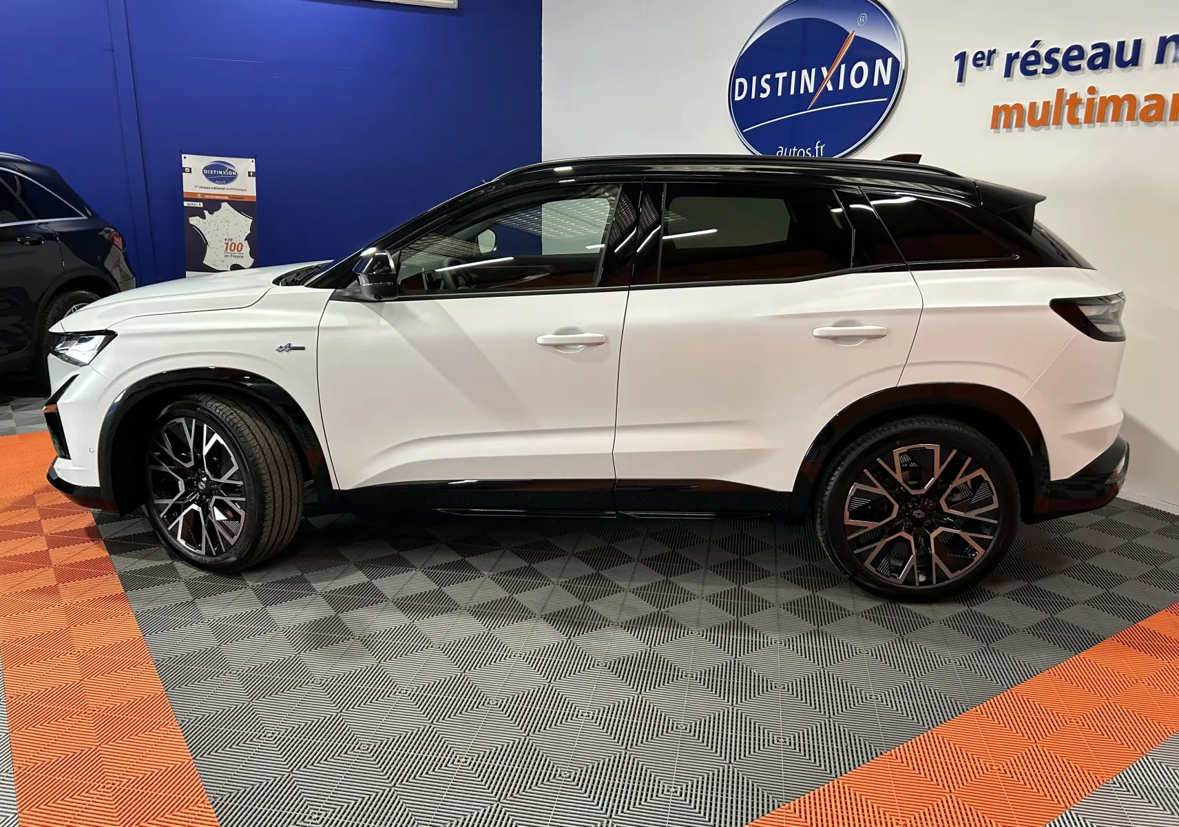 Vue latérale droite du Renault Austral blanc nacré satin avec toit noir et jantes bi-ton dans un showroom.