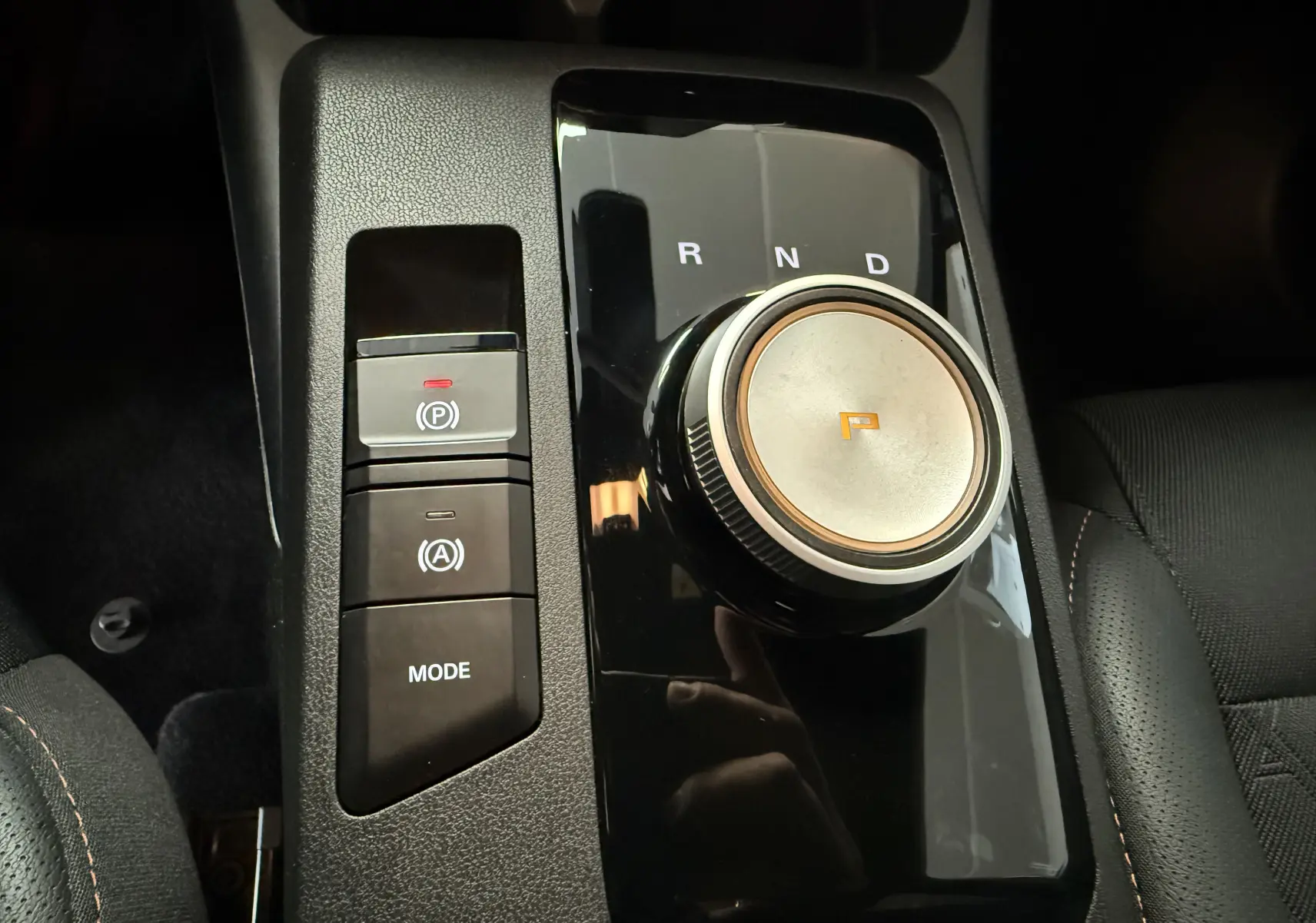 Gros plan sur la molette de boîte auto et commandes de mode en noir brillant, intérieur tissu et similicuir gris du MG3 2025.