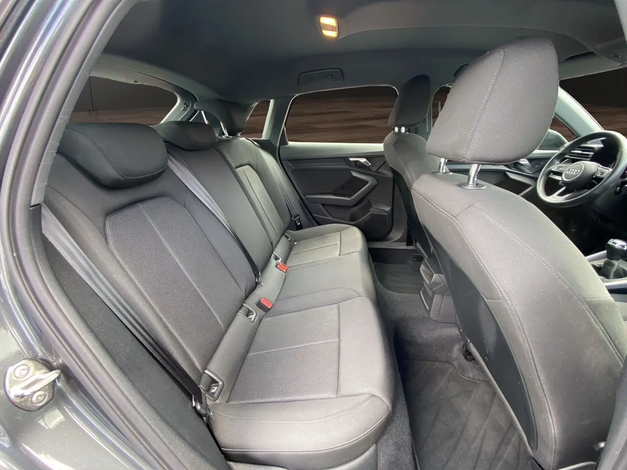 Intérieur arrière de l'Audi A3 Sportback gris Daytona, vue côté gauche avec sièges tissu noir et tableau de bord visible.