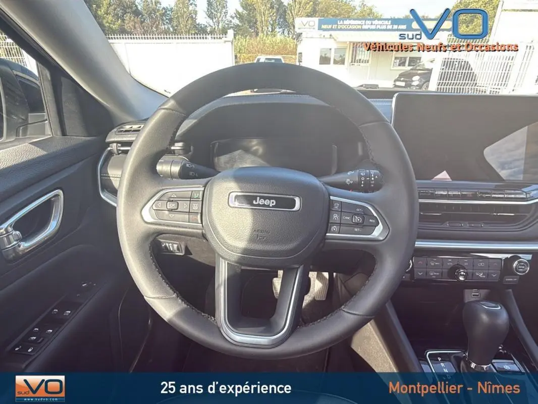 Vue centrée sur le volant Jeep d'un Compass blanc 2024, avec tableau de bord moderne et écran tactile visible à droite.