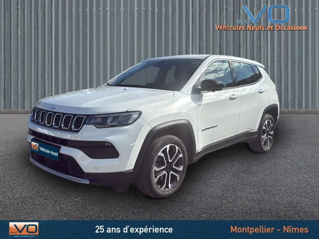 Jeep Compass blanc vue 3/4 avant droit, jantes alliage 18 pouces et calandre distinctive sur fond industriel.