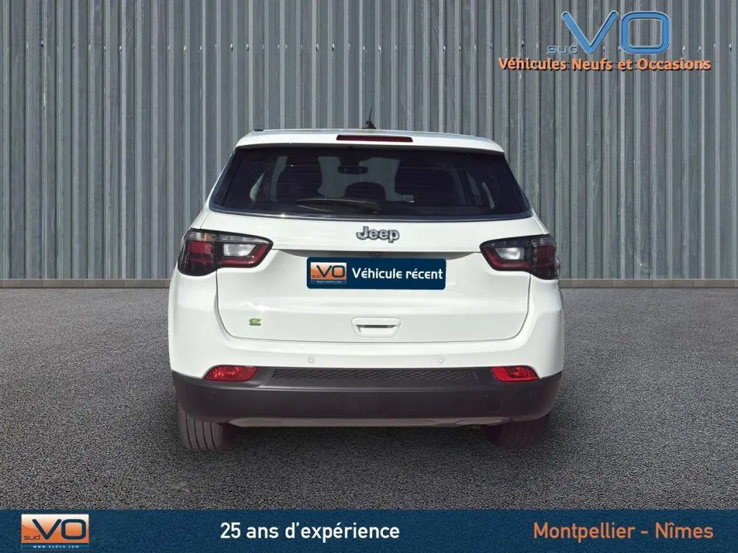 Vue arrière d'un Jeep Compass blanc 2024 avec feux arrière sombres et logo Jeep visible sur un sol gris.