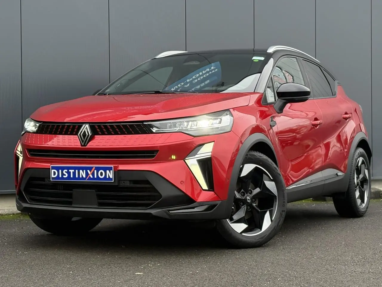 Renault Captur 2025 rouge flamme avec toit noir, vue 3/4 avant, jantes alu diamantées noires et phares LED allumés.