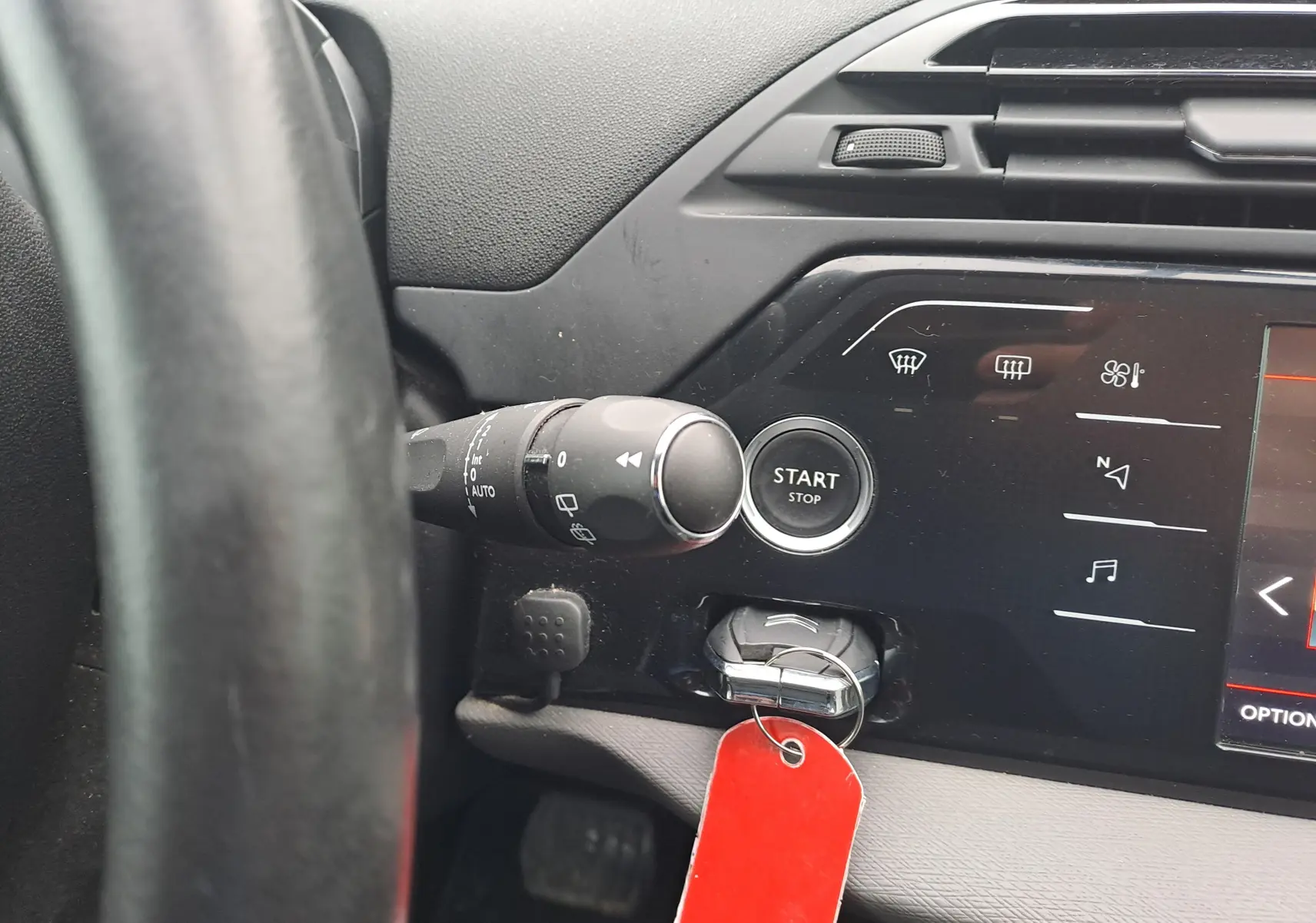 Gros plan sur le tableau de bord noir de la Citroën C4 Spacetourer avec bouton start/stop et clé à étiquette rouge.
