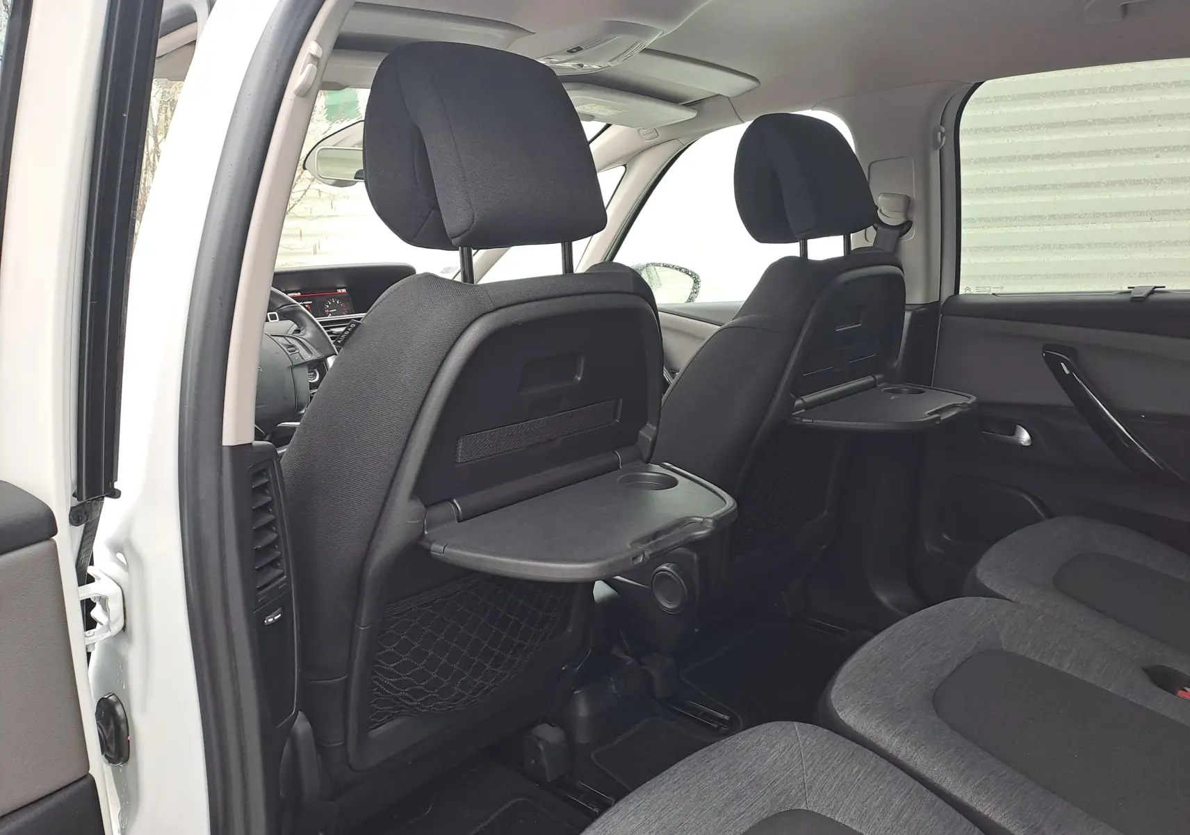 Vue intérieure arrière gauche du Citroën C4 Spacetourer blanc 2018, avec tablettes rabattables aux dossiers des sièges avant.