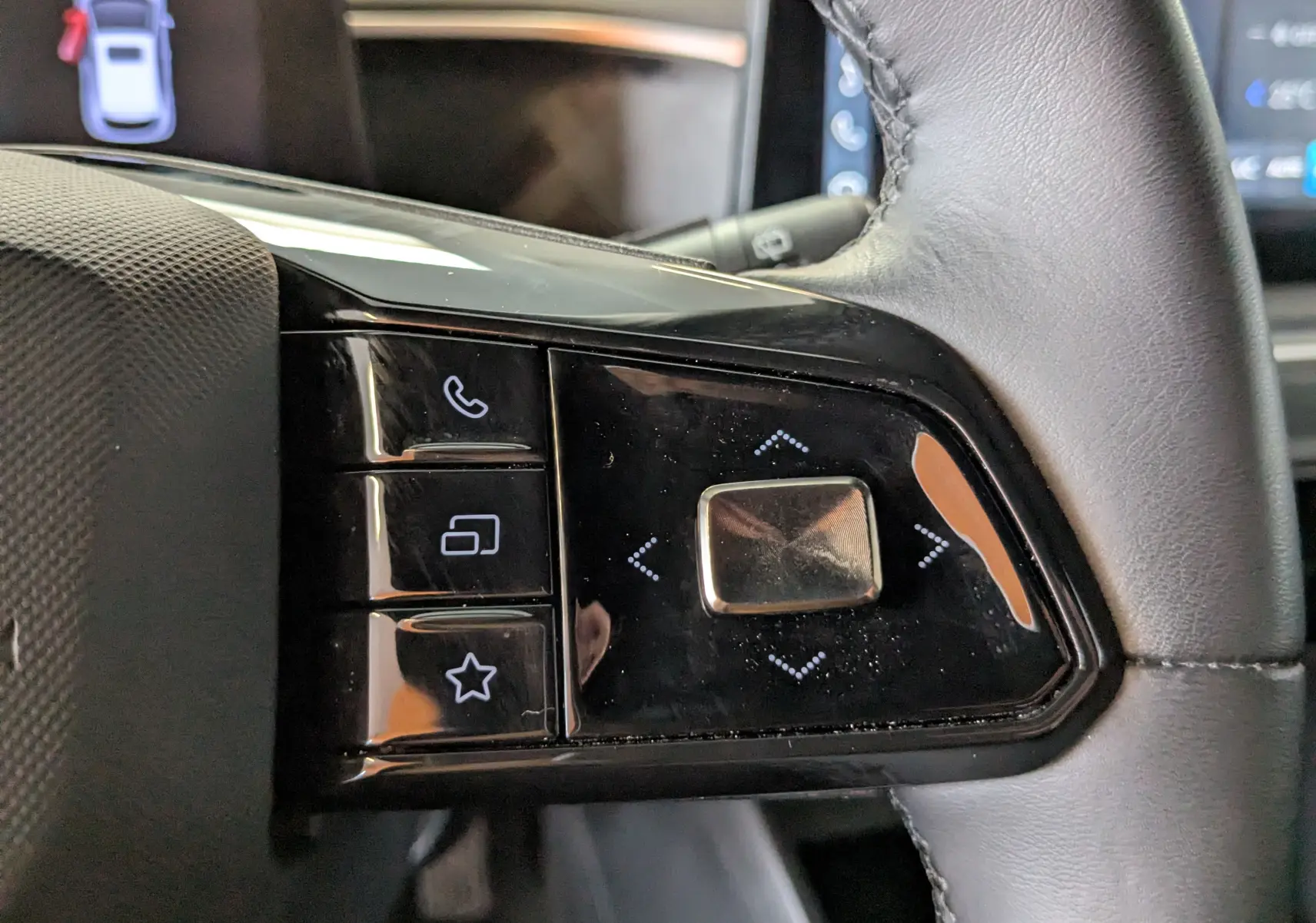 Gros plan sur les commandes noires du volant en cuir de la MG3 1.5 L Hybrid+ 2025, avec boutons tactiles et finition brillante.