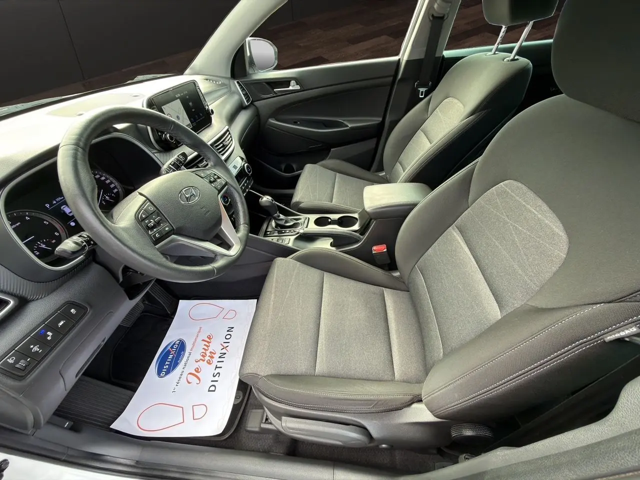 Vue intérieure côté conducteur du Hyundai Tucson 2020, sièges tissu noir et tableau de bord moderne.