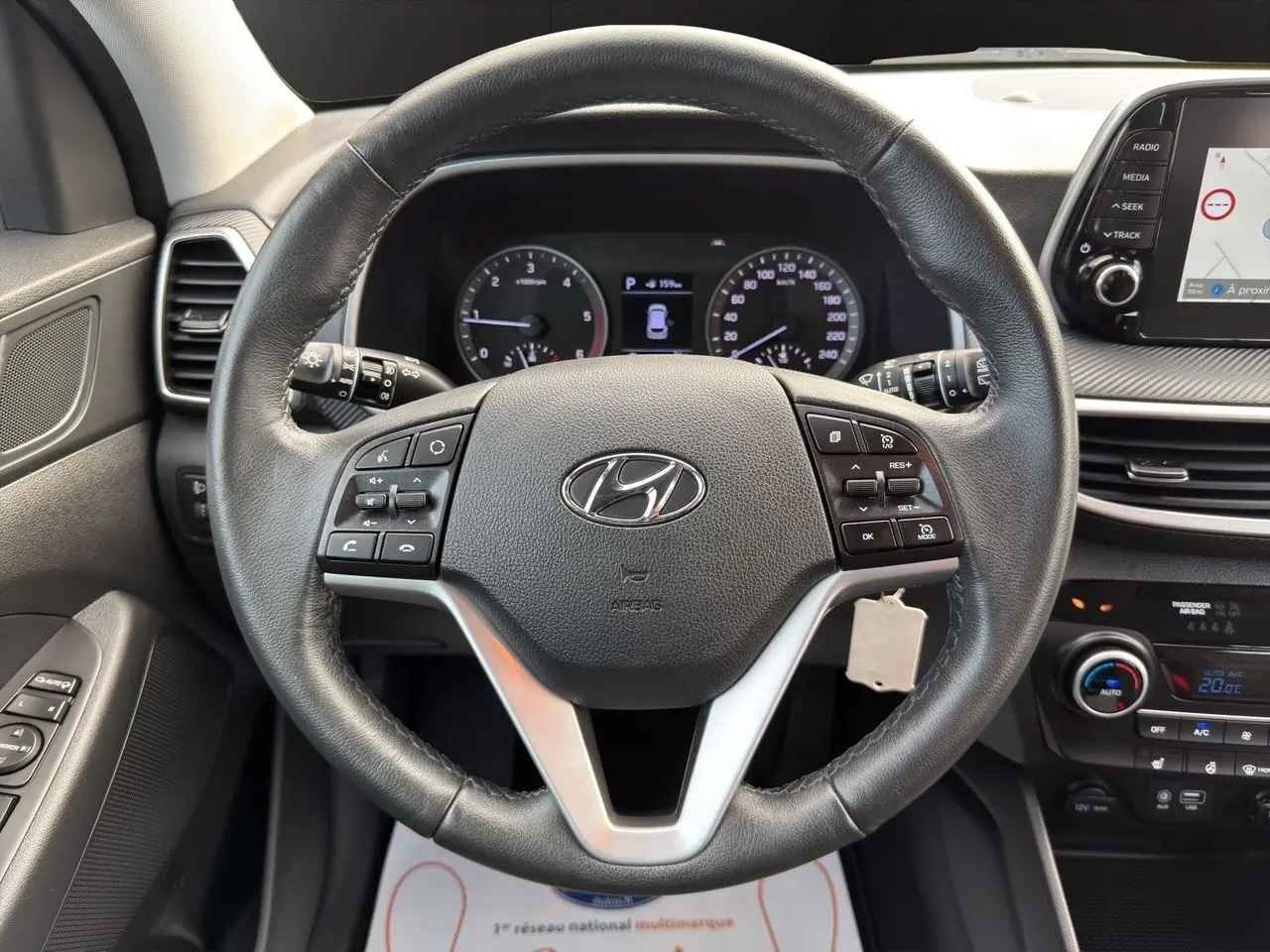 Vue rapprochée du volant en cuir noir d’un Hyundai Tucson 2020 avec commandes intégrées et tableau de bord numérique.