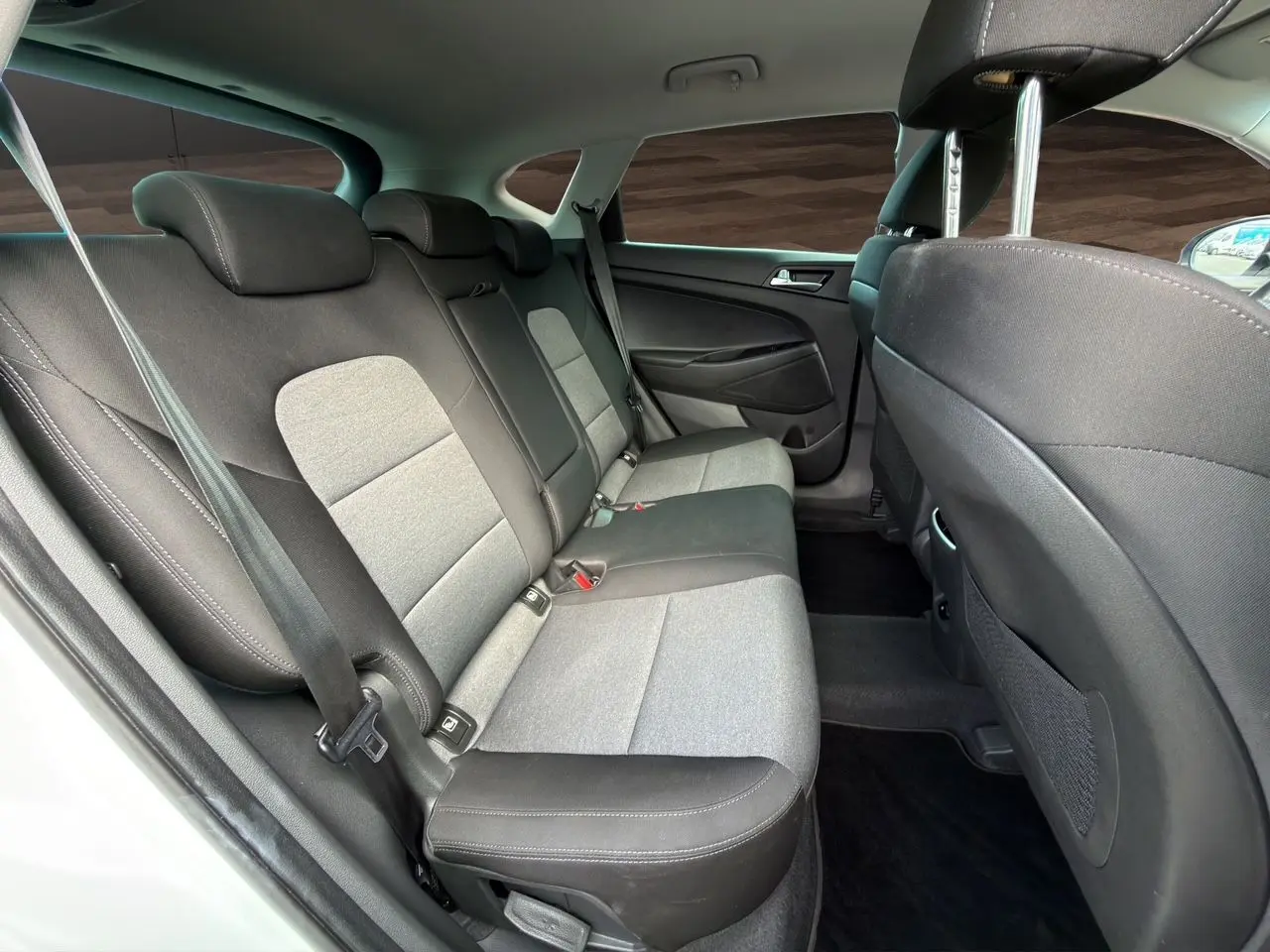 Vue intérieure arrière côté gauche du Hyundai Tucson blanc polar 2020, sièges tissu noir et gris avec ceintures de sécurité visibles.