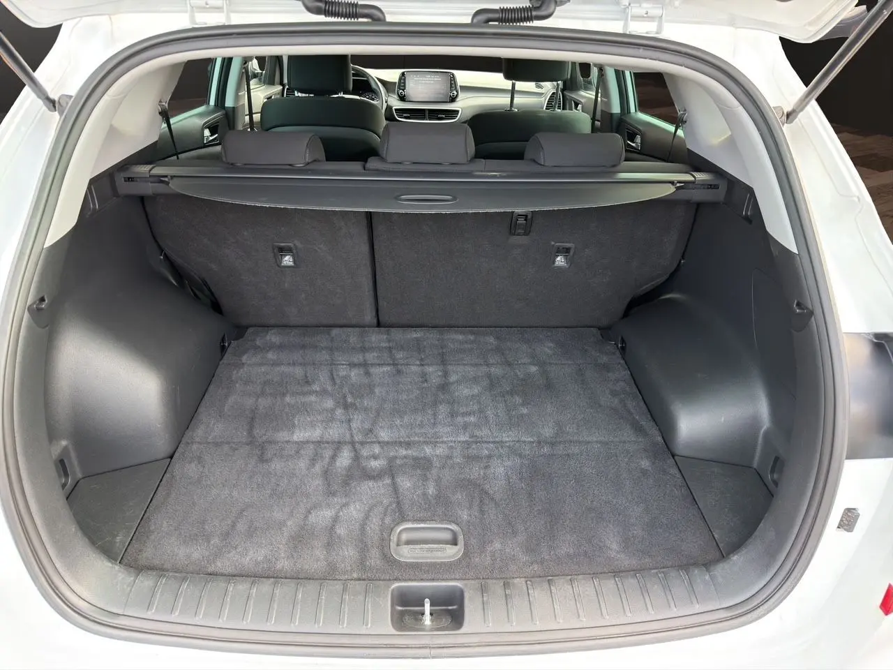 Coffre ouvert du Hyundai Tucson blanc polar 2020, vue arrière montrant l'espace de chargement et la banquette arrière noire.