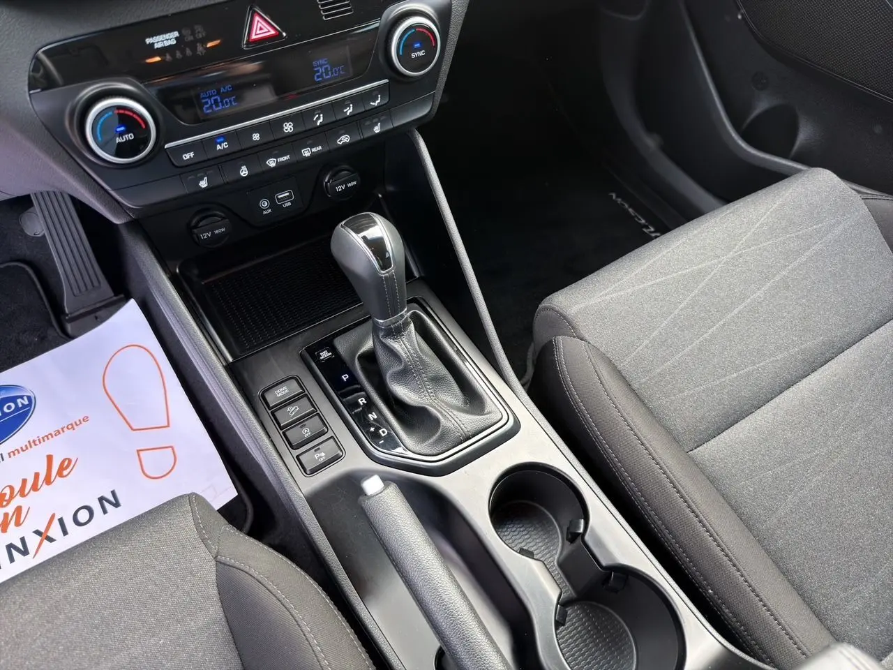 Vue intérieure centrée sur la console centrale du Hyundai Tucson 2020, avec levier de vitesse automatique et sièges tissu gris.